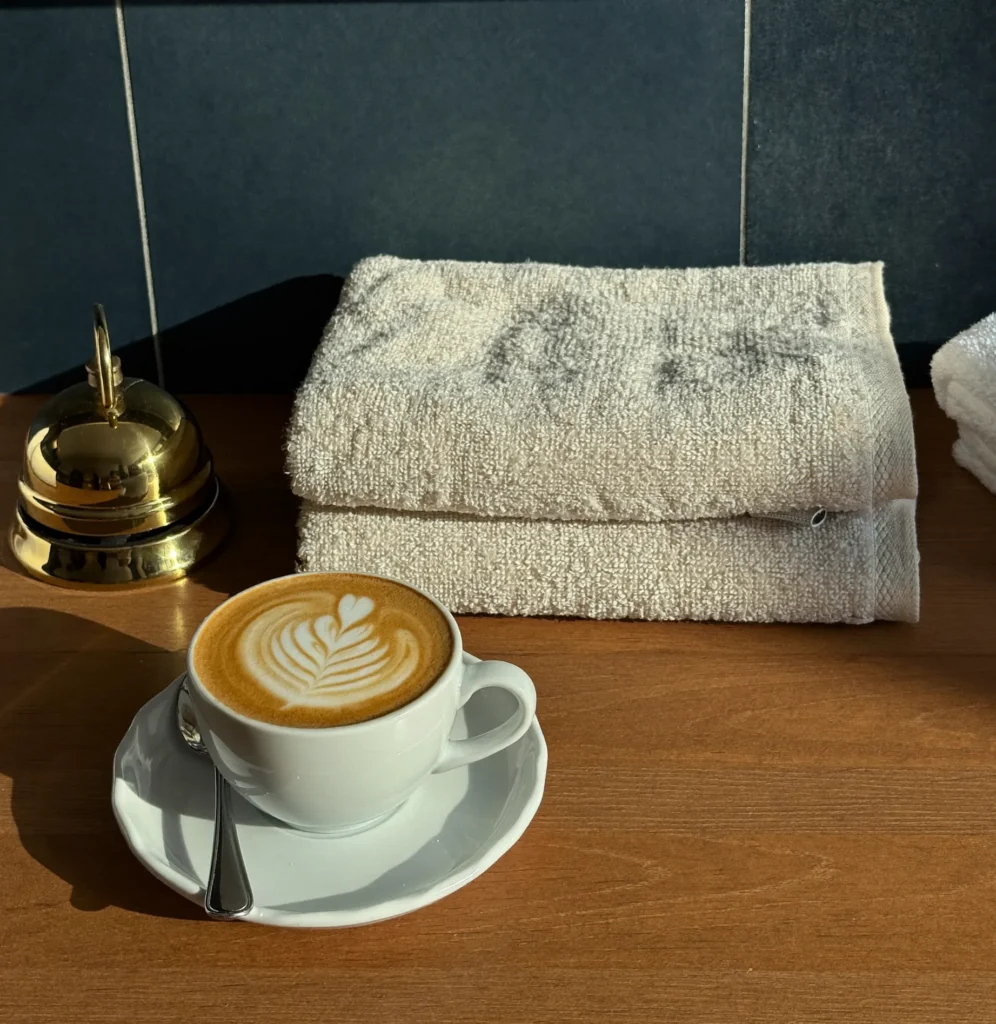Cappuccino naast gevouwen handdoeken en een koperen belletje op de toonbank