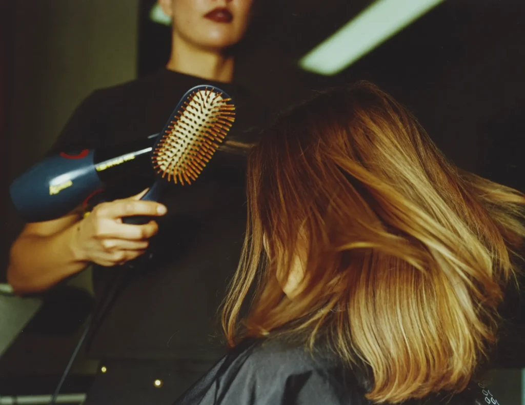 Kapster föhnt schouderlang blond haar met een ronde borstel