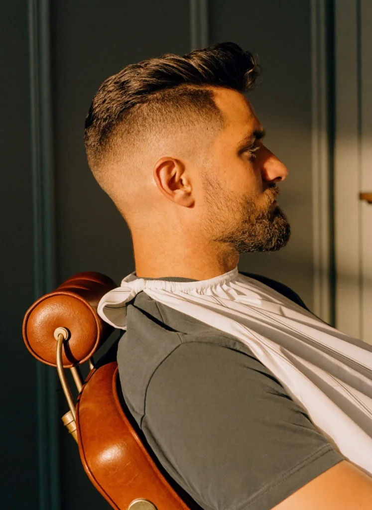 Man with a skin fade and beard in the barber chair, side view