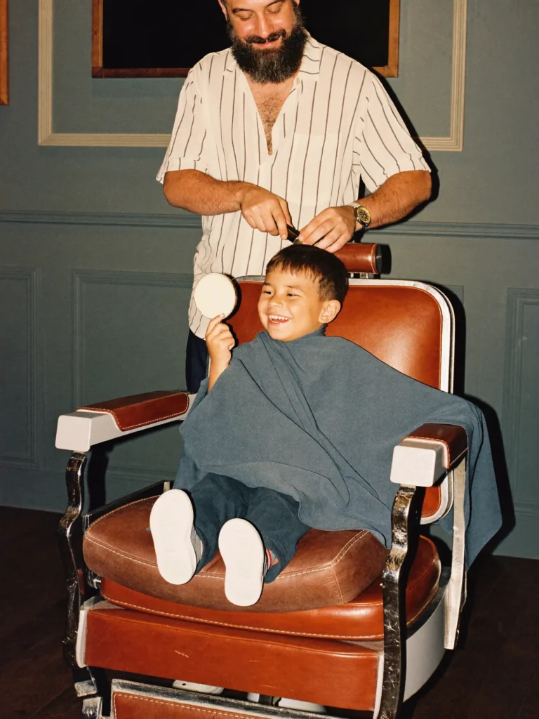 Happy little boy holding a hand mirror in the salon chair during his haircut